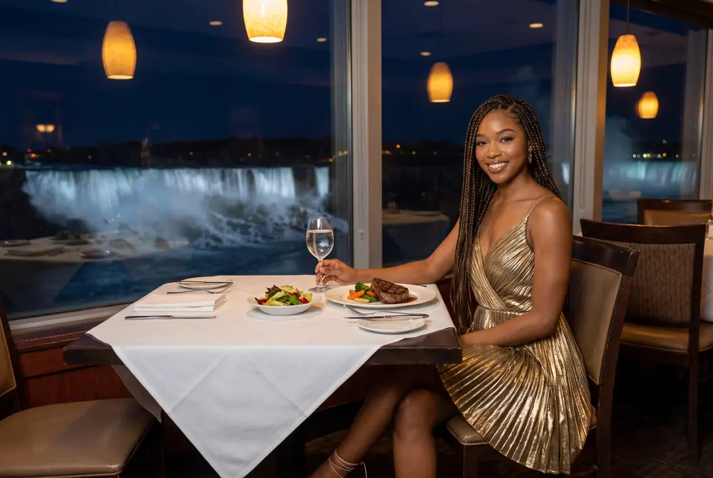 Simone Ashby, a character created for this guide, at a steakhouse table with a plated steak and a glass of sparkling water, the lit falls in the window; AI-generated image.